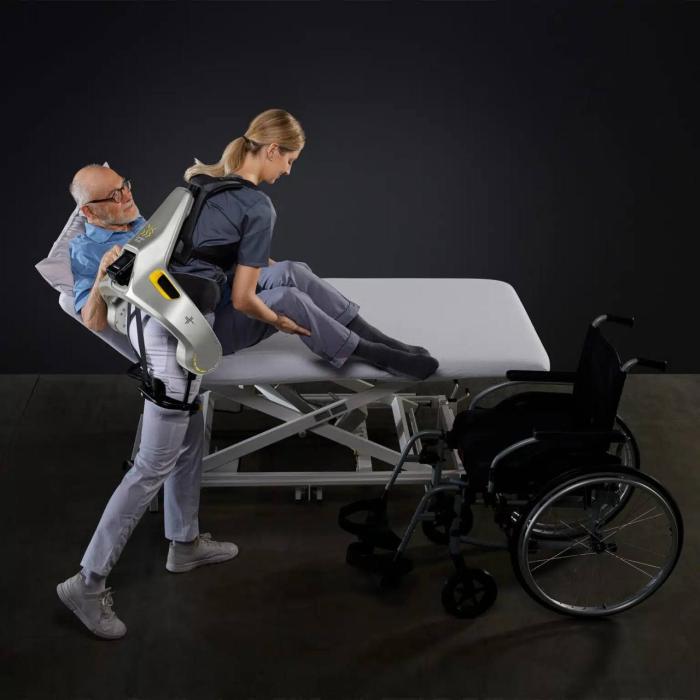 간병 인력이 German Bionic사에서 개발한 웨어러블 로봇 아포지플러스Apogee를 입고 노인을 침대에서 휠체어로 옮기고 있다